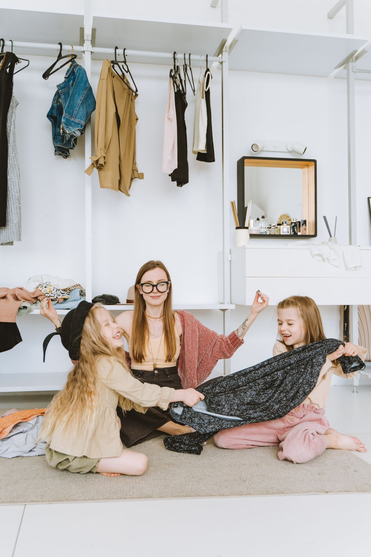 Twee kinderen passen kleding uit de kast met hulp van een volwassene