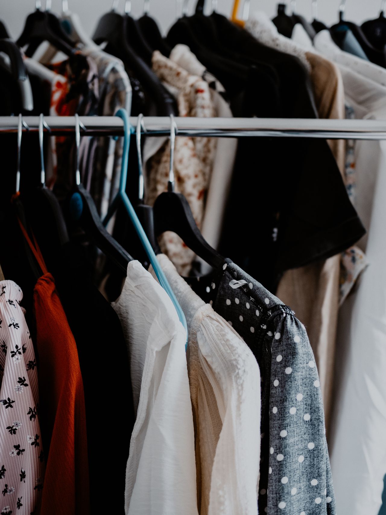 Kledingrek met blouses en jurken op hangers in wit, zwart, roest en stippen