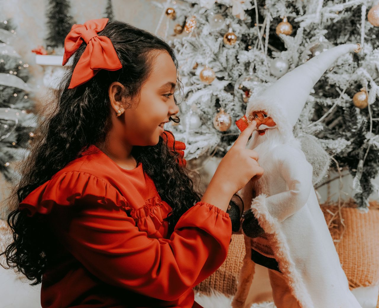 Meisje in rode kerstjurk speelt met een kerstman-pop bij de kerstboom