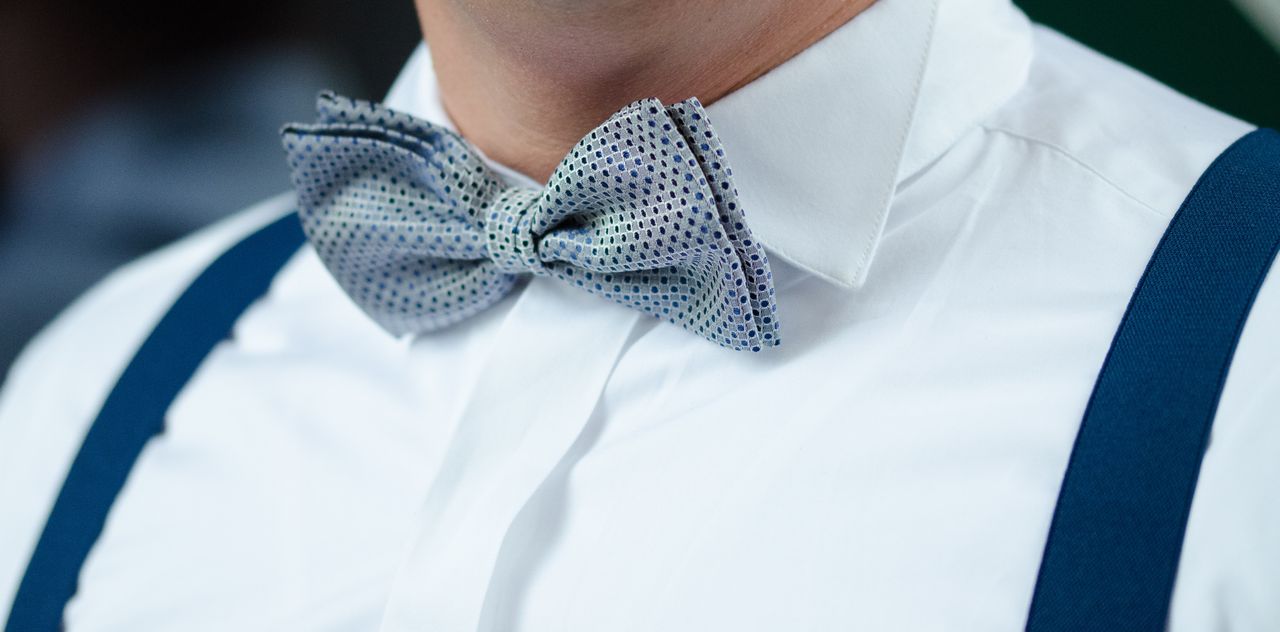 Close-up van een gestipte vlinderdas bij een witte kraag en blauwe bretels