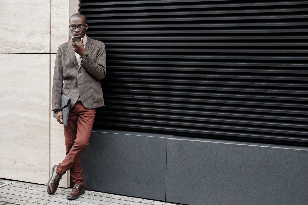 Man tegen muur leunend in smart casual outfit